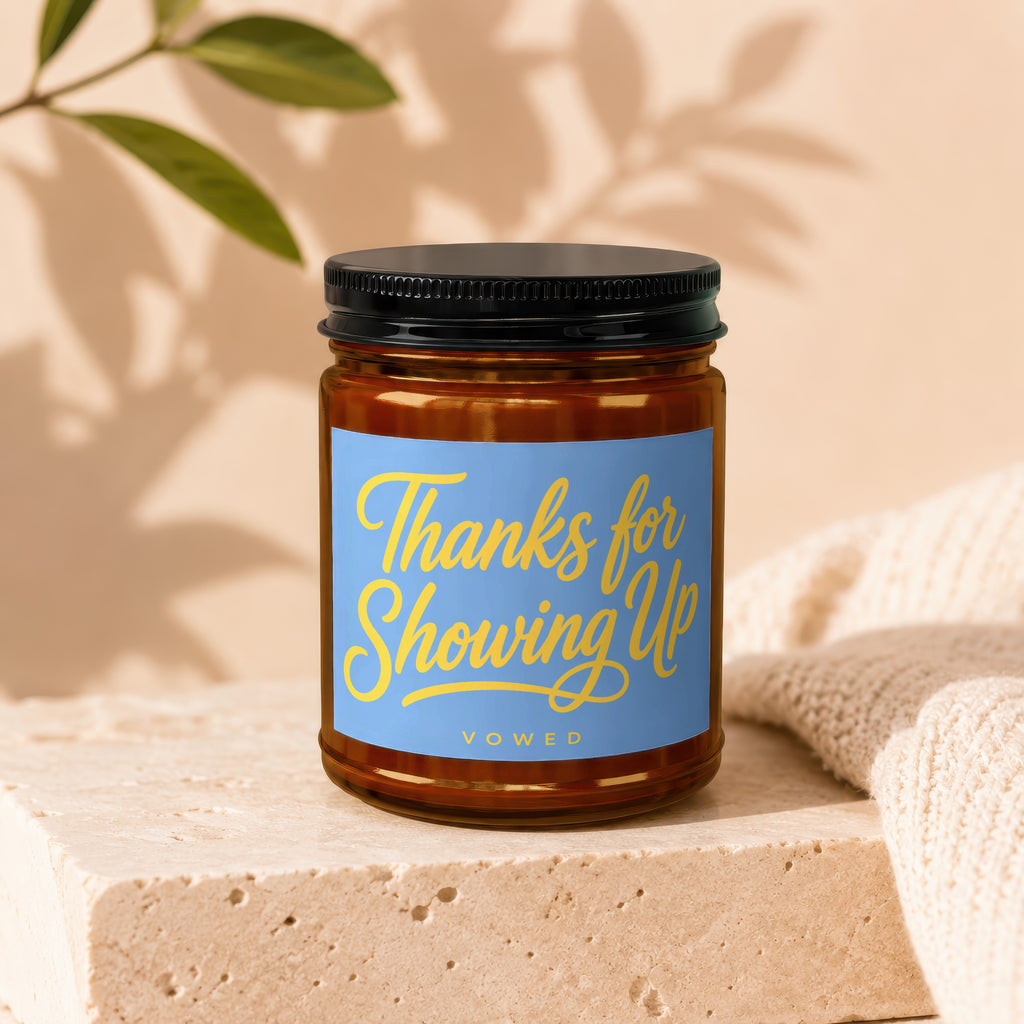 Amber glass candle with a blue label that reads "Thanks for Showing Up Vowed."