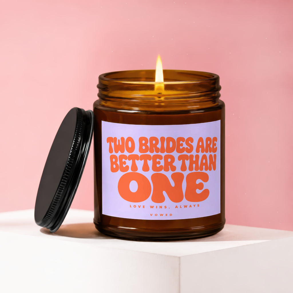 Amber jar candle with lit flame and lid off, text reads "TWO BRIDES ARE BETTER THAN ONE".