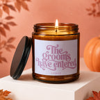 Amber glass candle with lit wick and lid, reads "The grooms have entered VOWED".