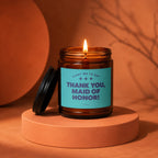 Lit candle in amber jar with "Thank You, Maid of Honor!" text on turquoise label.