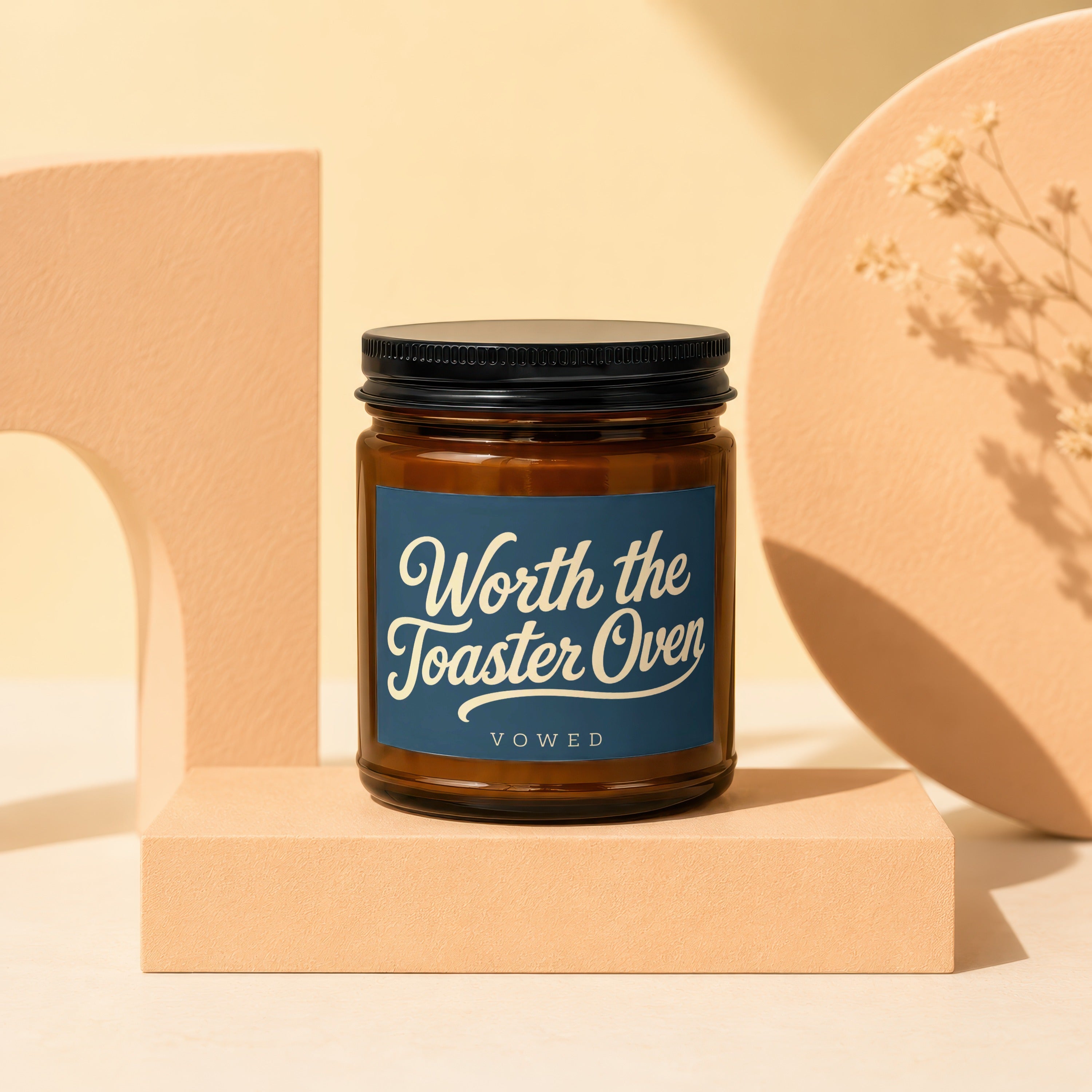 Brown glass candle with dark blue label reading "Worth the Toaster Oven" and "VOWED".