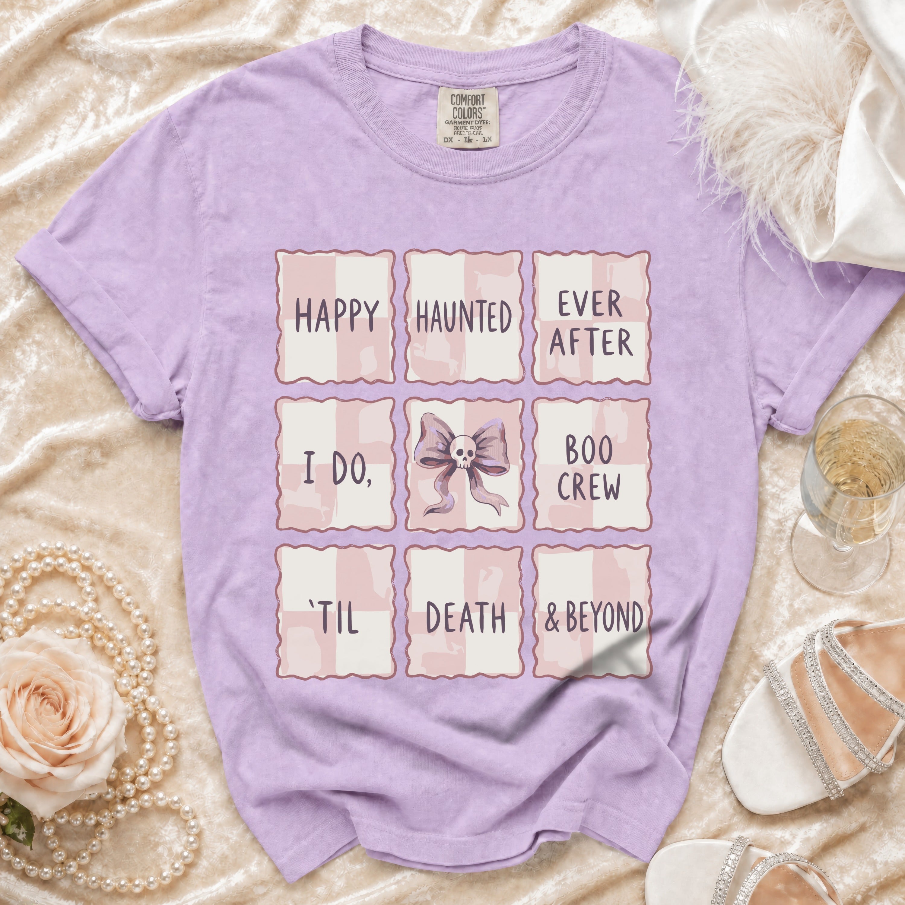 Lavender Comfort Colors t-shirt with grid design featuring "Happy Haunted Ever After," "I Do," skull bow, "Boo Crew," "'Til Death & Beyond."