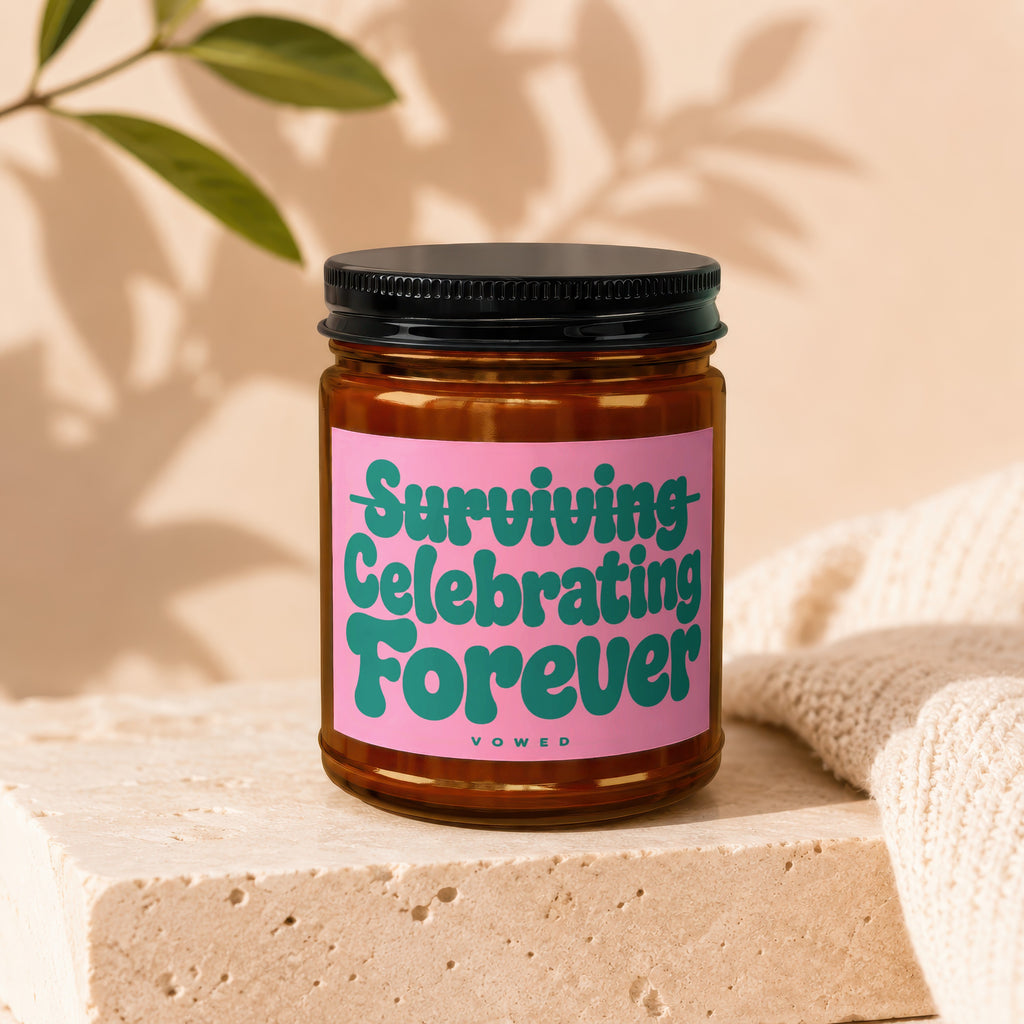 Brown glass candle with pink label reading "Surviving Celebrating Forever Vowed".