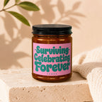 Brown glass candle with pink label reading "Surviving Celebrating Forever Vowed".