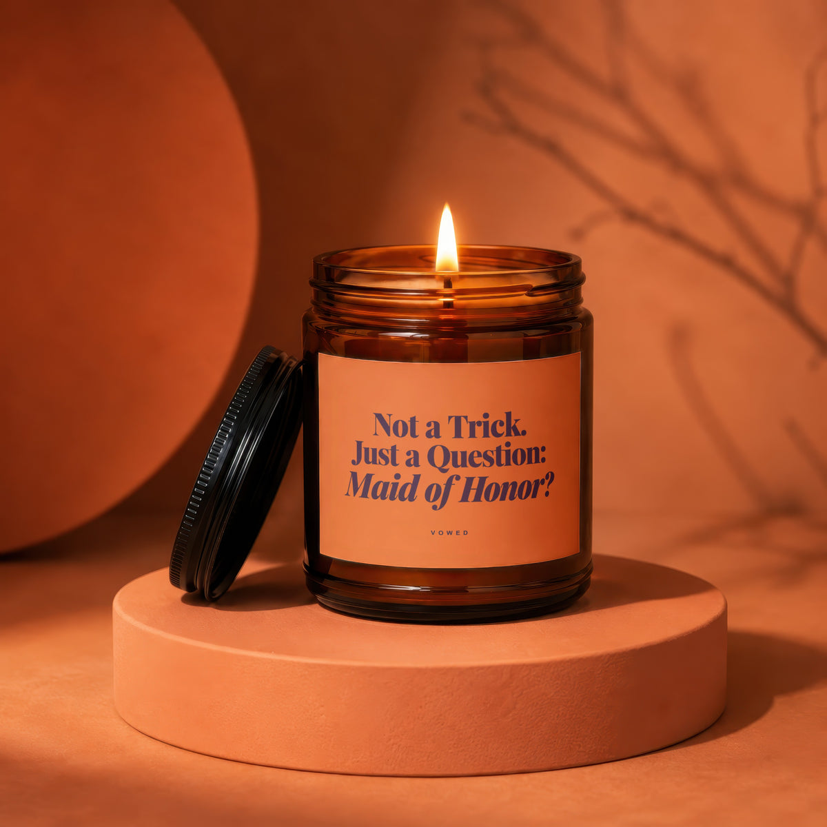 Amber jar candle with lit flame, reads "Not a Trick. Just a Question: Maid of Honor?"