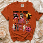 Orange t-shirt with "Mother of the Bride Raising Hell Before the I Do" Halloween graphic.