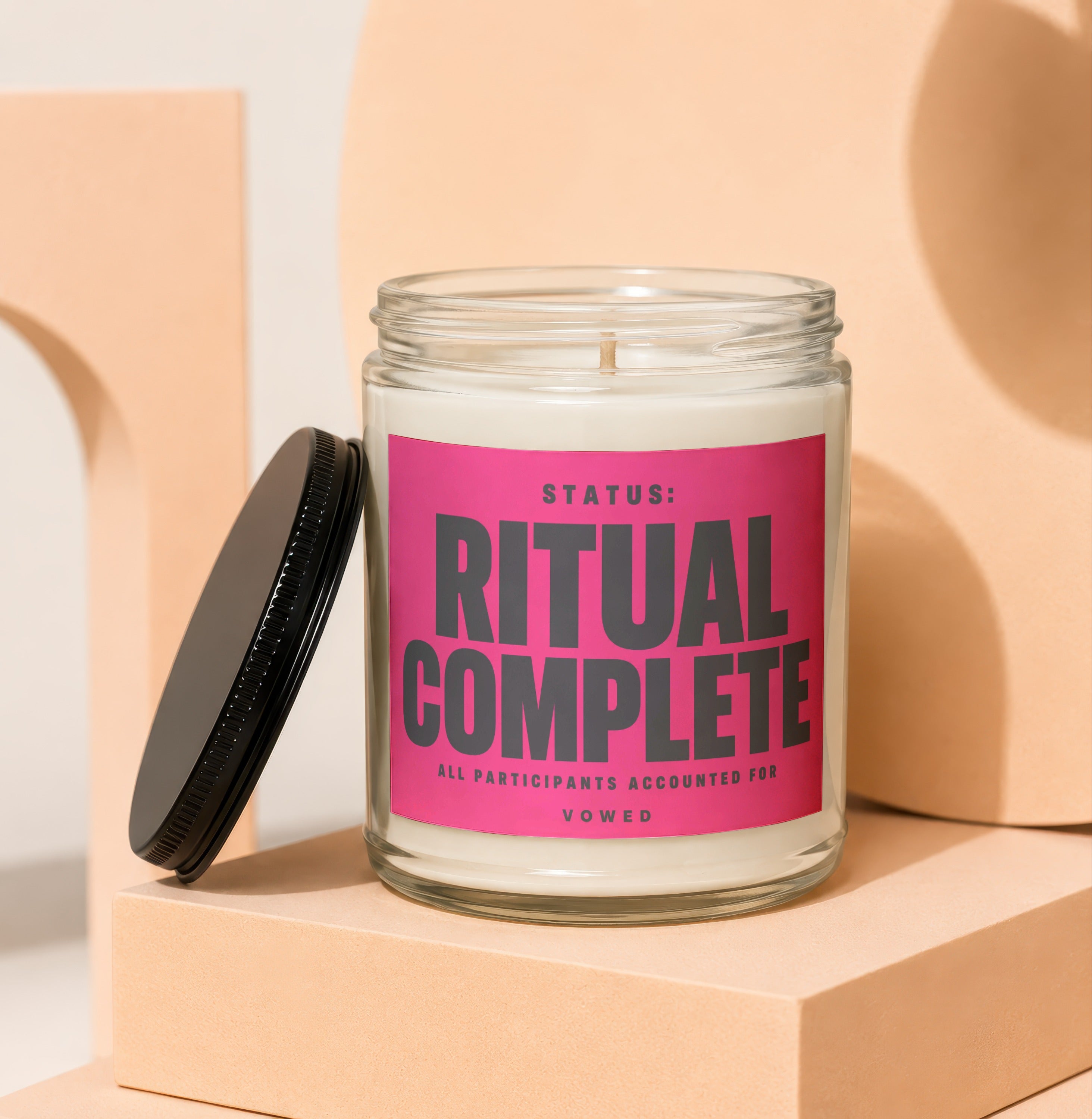 Glass jar candle with "STATUS: RITUAL COMPLETE" text on pink label.
