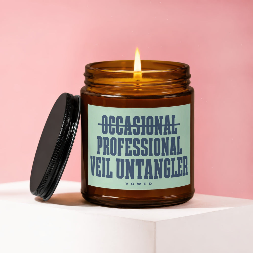 Amber jar candle with a lit flame and black lid, featuring text: Occasional Professional Veil Untangler.