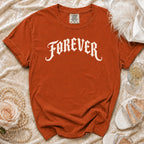 Orange t-shirt with "FOREVER" printed in white gothic font, styled with pearls and heels.