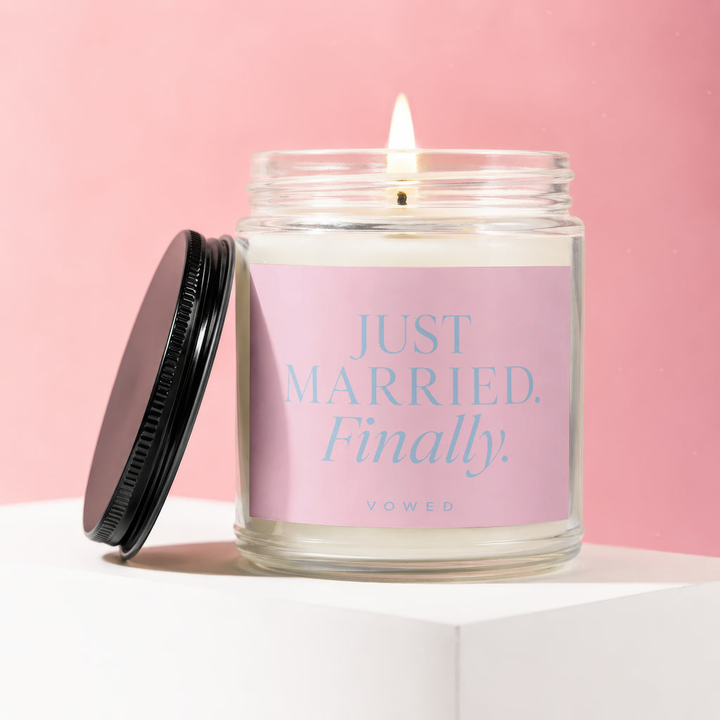 Candle with "JUST MARRIED. Finally" text, lid off, on white pedestal.