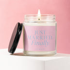 Candle with "JUST MARRIED. Finally" text, lid off, on white pedestal.