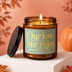 Lit amber jar candle with black lid surrounded by autumn leaves, reads "Our love, our rules. VOWED".