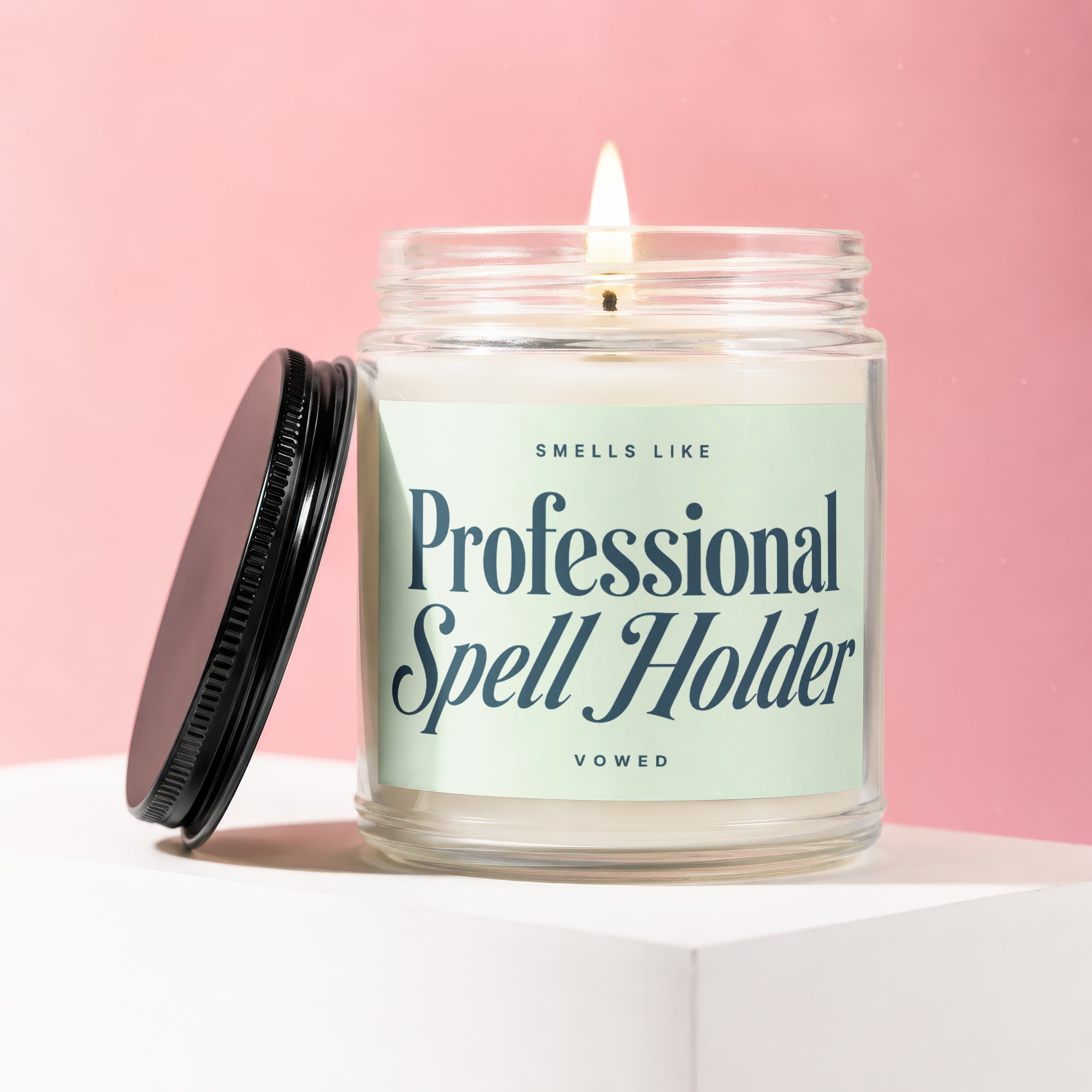 Lit scented candle in glass jar with black lid, "Professional Spell Holder" label.