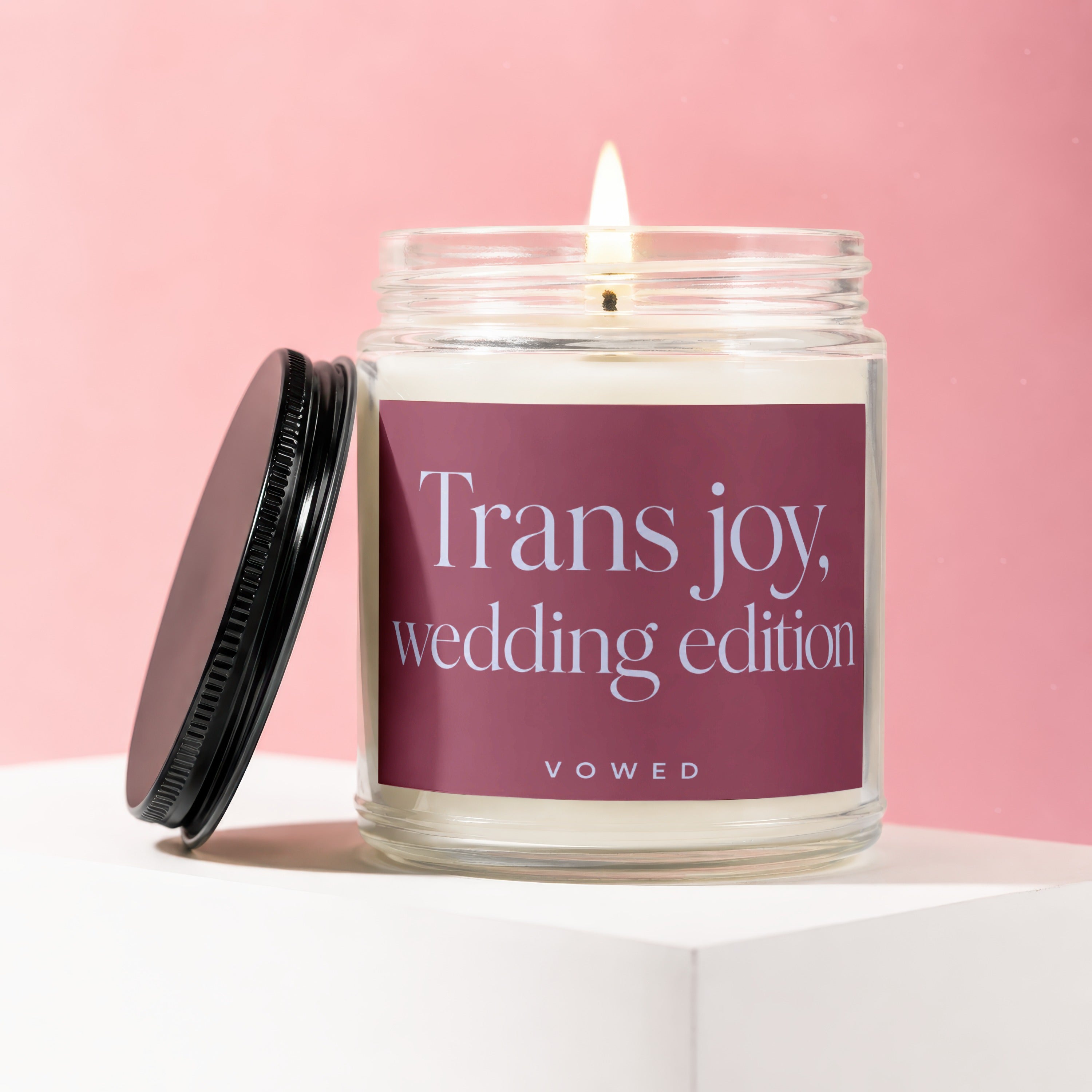 Glass candle with lit wick, "Trans joy, wedding edition" text on label.