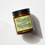Amber glass candle with a lime-green label reading "Ringed and Radiant" and "vowed".