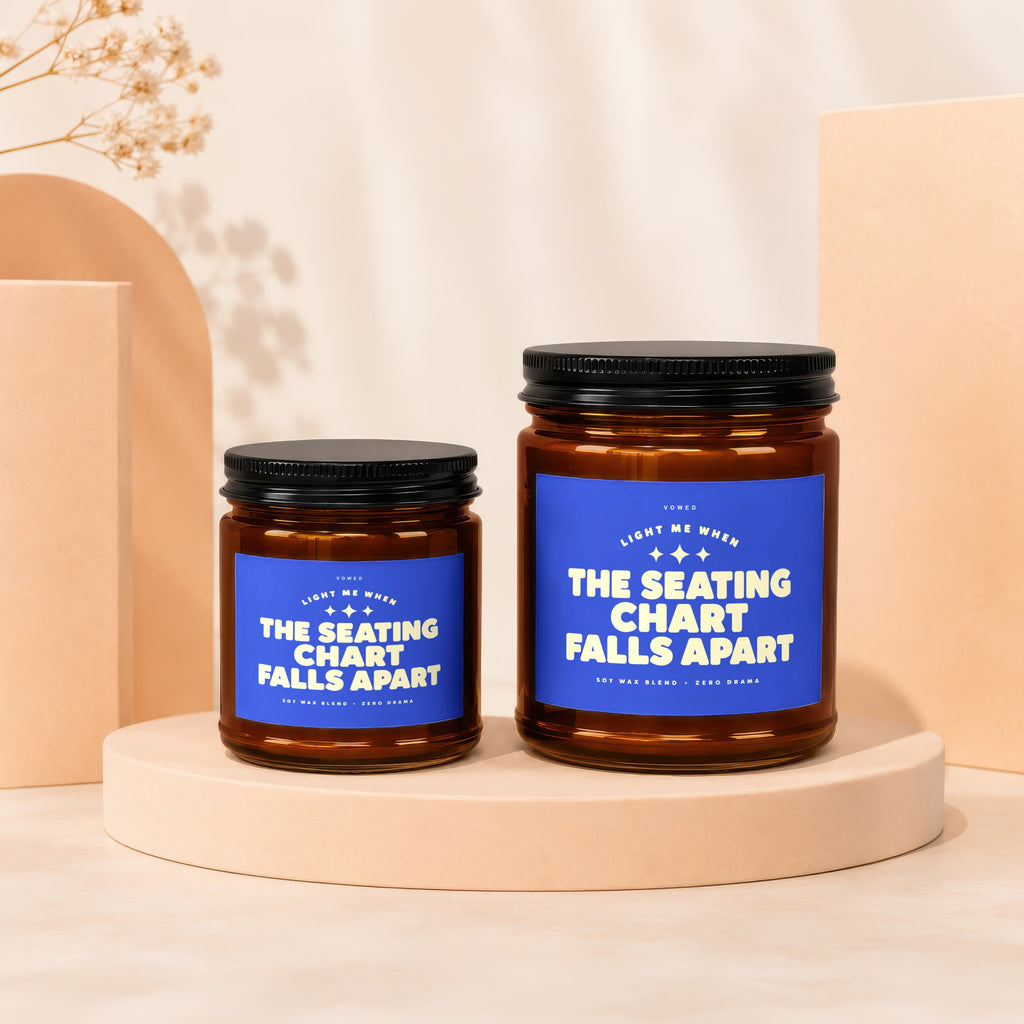 Two amber glass candles with blue labels reading "The Seating Chart Falls Apart".