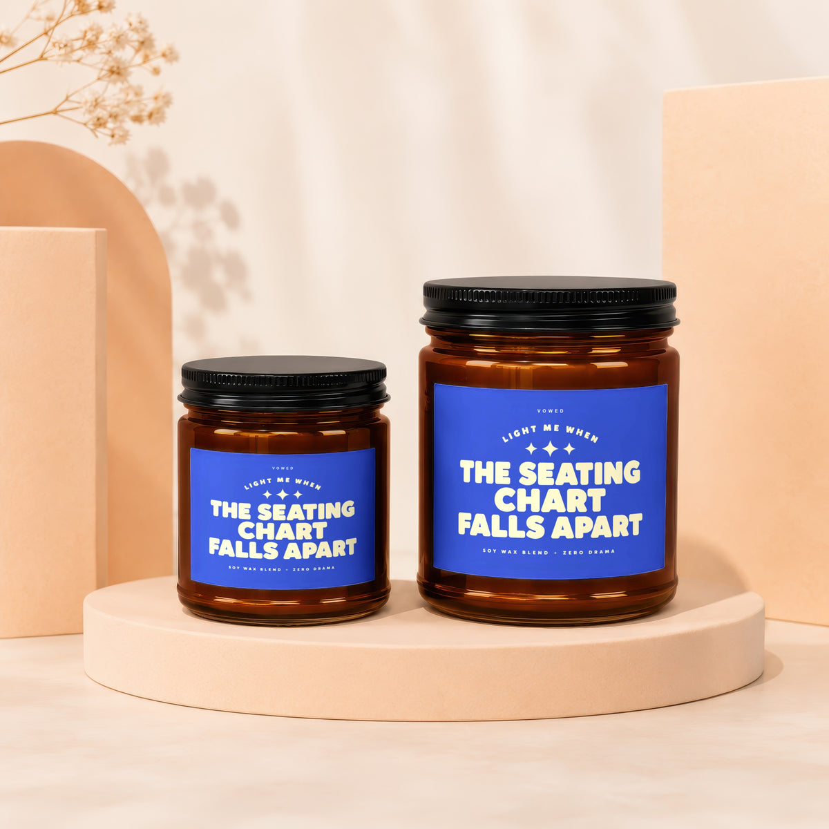 Two amber glass candles with blue labels reading "The Seating Chart Falls Apart".