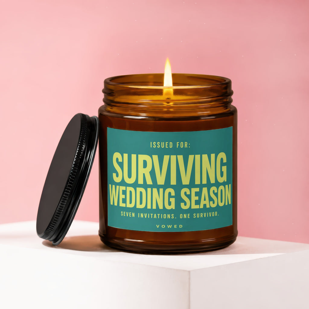 Amber jar candle with lit flame and teal label reading "Surviving Wedding Season."