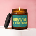 Amber jar candle with lit flame and teal label reading "Surviving Wedding Season."