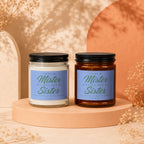 Two scented candles, one white and one amber, with "I Found My Mister, But I Still Need My Sister" text.