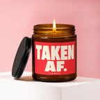 Amber jar candle with lit wick and red label reading "TAKEN AF. VOWED."