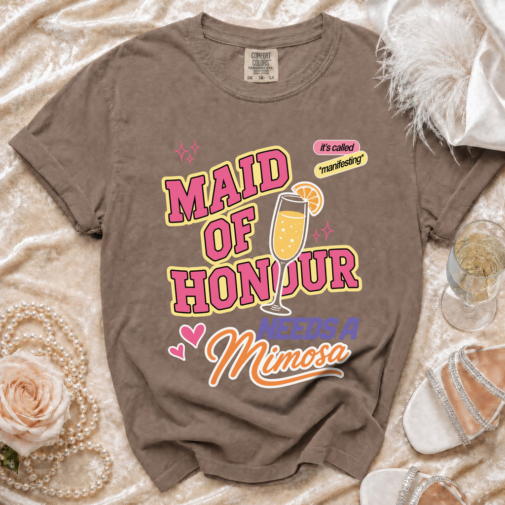 Brown t-shirt with "Maid of Honour Needs a Mimosa" graphic and champagne glass.