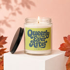 Glass jar candle with lid off, lit wick, and "Queerly Ever After VOWED" label.