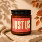Brown candle with "JUST US" on the label, next to knitted fabric.