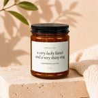 Candle with text: "Smells like a very lucky fiancé and a very shiny ring."