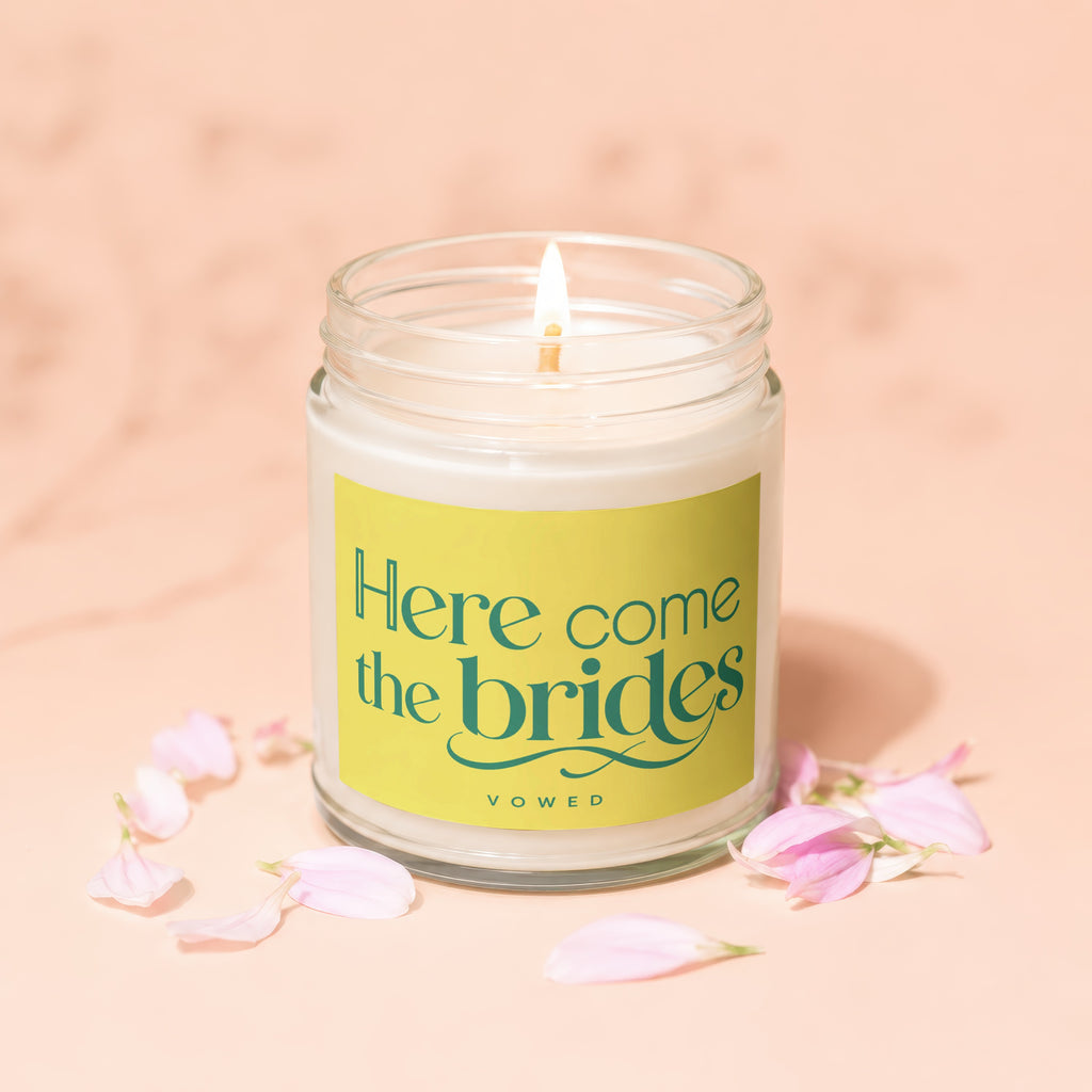 Jar candle with lit wick and "Here come the brides" text on yellow label.