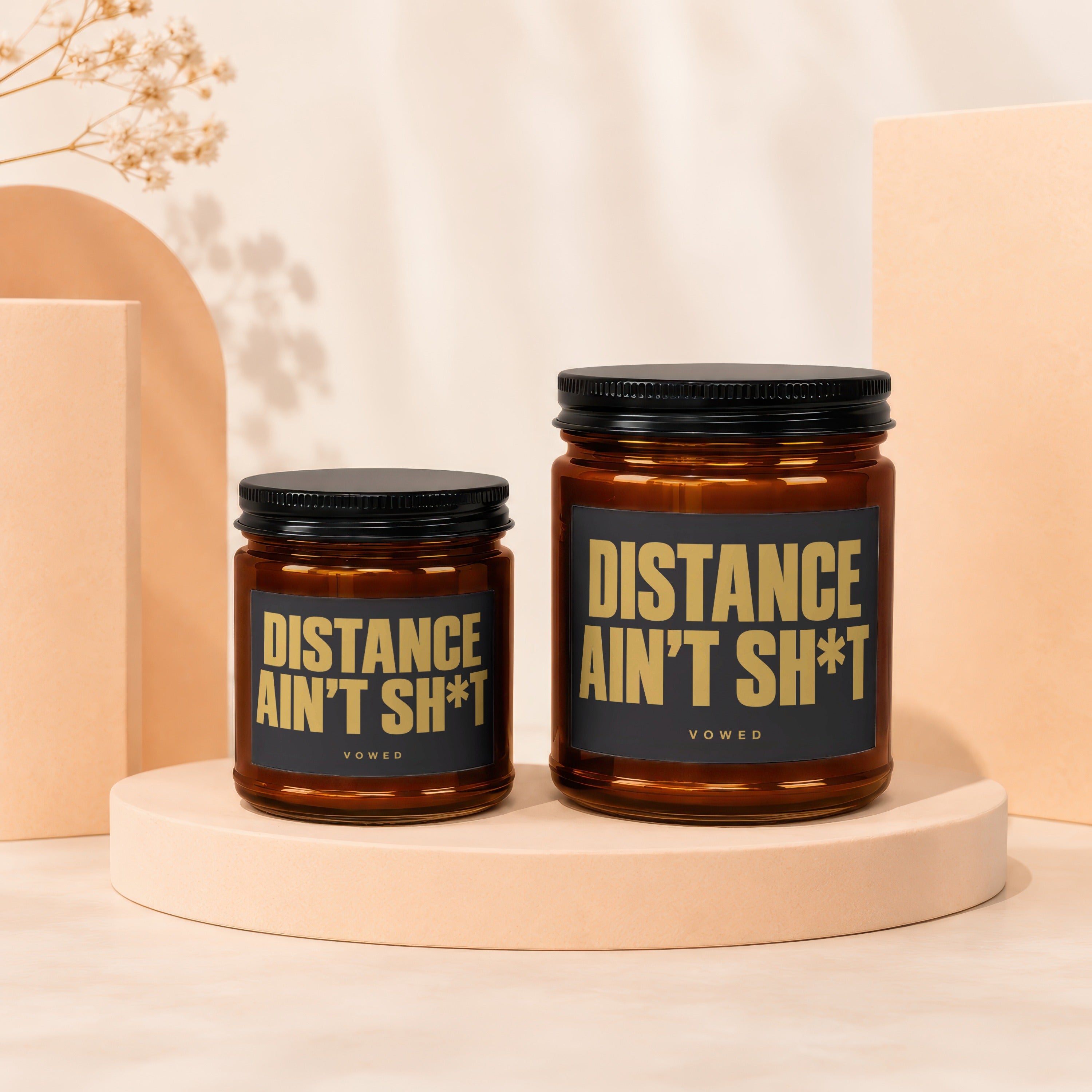 Two amber glass candles with black lids and black labels saying "DISTANCE AIN'T SH*T".