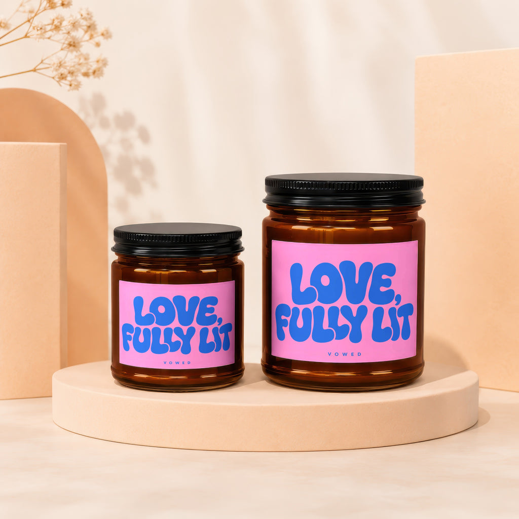 Two amber glass candles with pink labels reading "LOVE, FULLY LIT"
