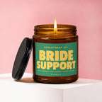 Amber jar candle with lit flame, green label reads "Bride Support".