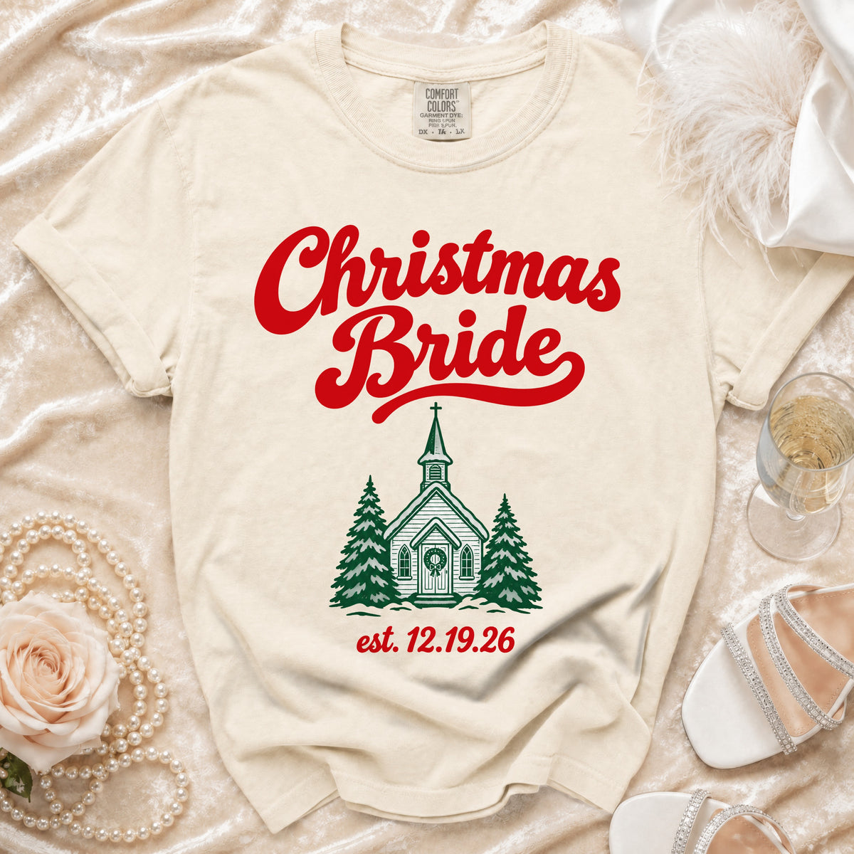Cream t-shirt featuring red script text reading "Christmas Bride", a green church graphic, and the date "est. 12.19.26".