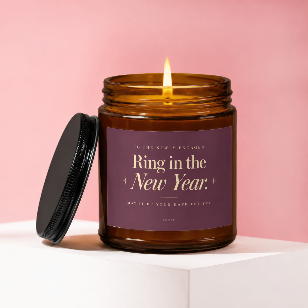 Amber jar candle with lit flame reads "Ring in the New Year. May it be your happiest yet."