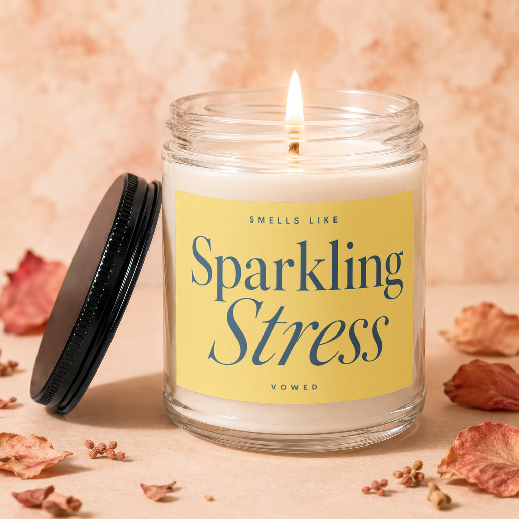 Candle with lit wick and label reading "Smells Like Sparkling Stress"