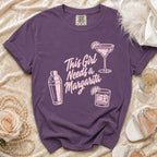 Purple t-shirt with "This Girl Needs a Margarita" text and drink illustrations.