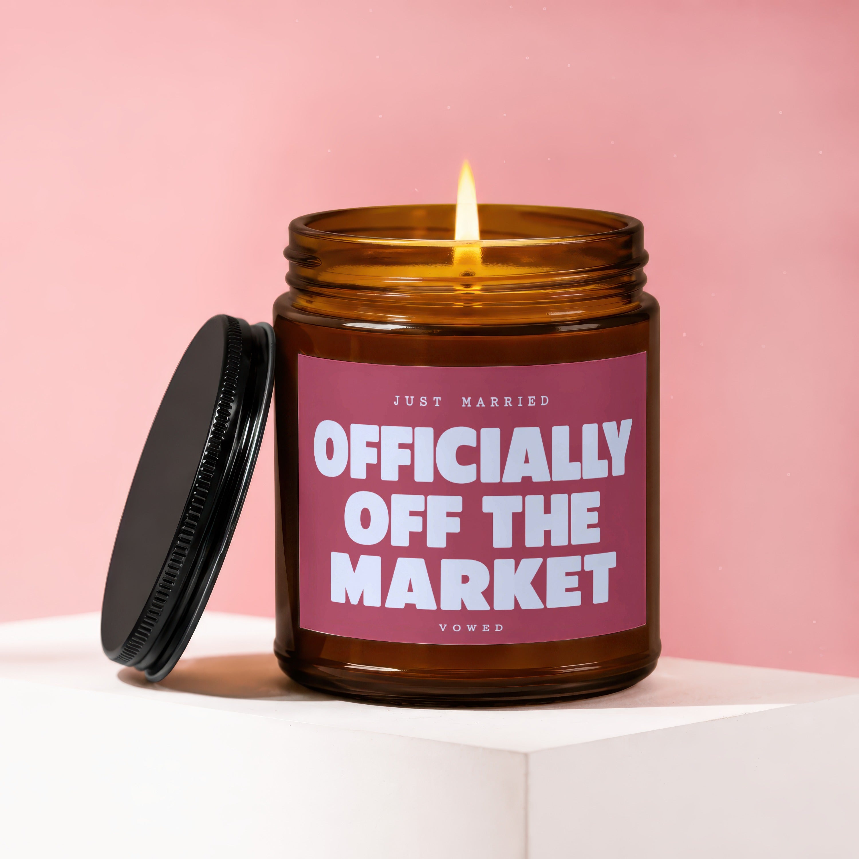 Amber jar candle with lit wick, lid off, reads "JUST MARRIED OFFICIALLY OFF THE MARKET VOWED".