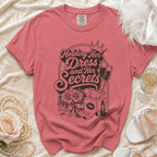 Pink t-shirt with "Holding Her Dress and Her Secrets" graphic and icons.