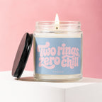 Candle with pink text "Two rings, zero chill" on blue label in glass jar.