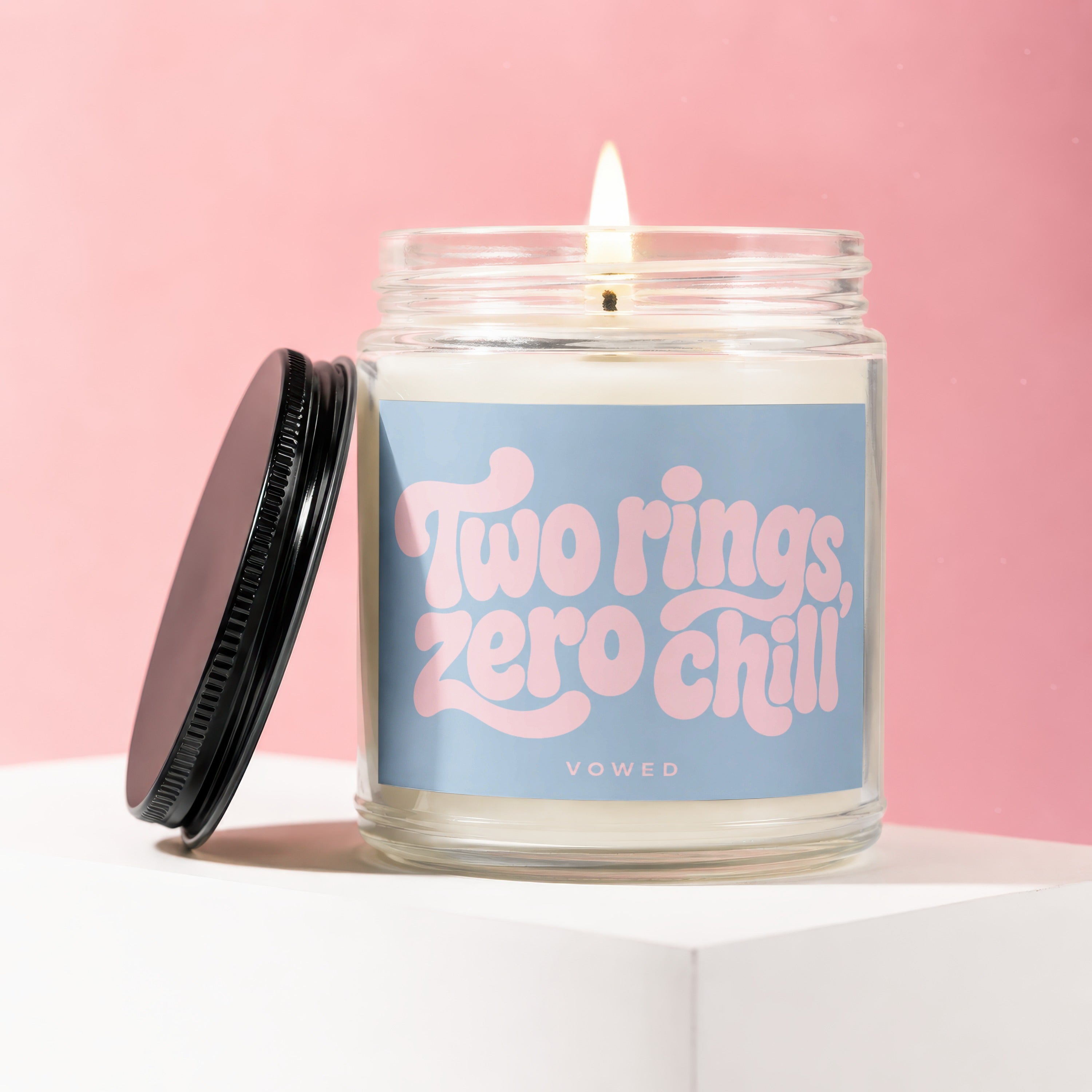 Candle with pink text "Two rings, zero chill" on blue label in glass jar.