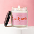 Burning candle in glass jar with pink label reading "Smells Like Nearlyweds"
