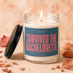 Lit glass candle with "Survived The Bachelorette" text on the label, lid to the side.