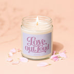 Glass jar candle with a lit wick and a "Love, out loud" label surrounded by flower petals.