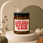 Amber jar candle with black lid and label reading "SHE SAID YES VOWED".