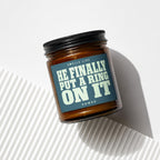 Amber jar candle with black lid and label reading "Smells Like He Finally Put A Ring On It Vowed".