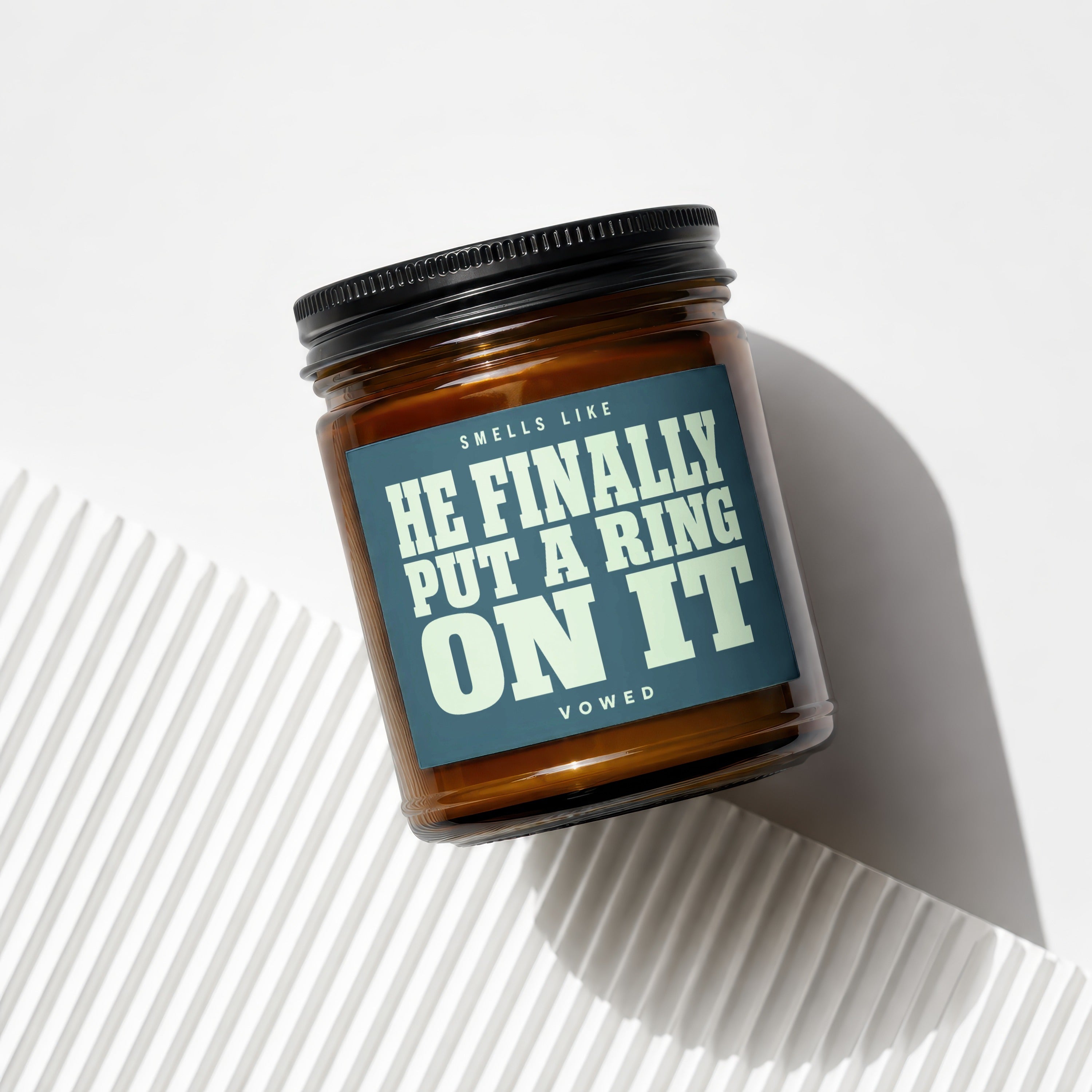 Amber jar candle with black lid and label reading "Smells Like He Finally Put A Ring On It Vowed".