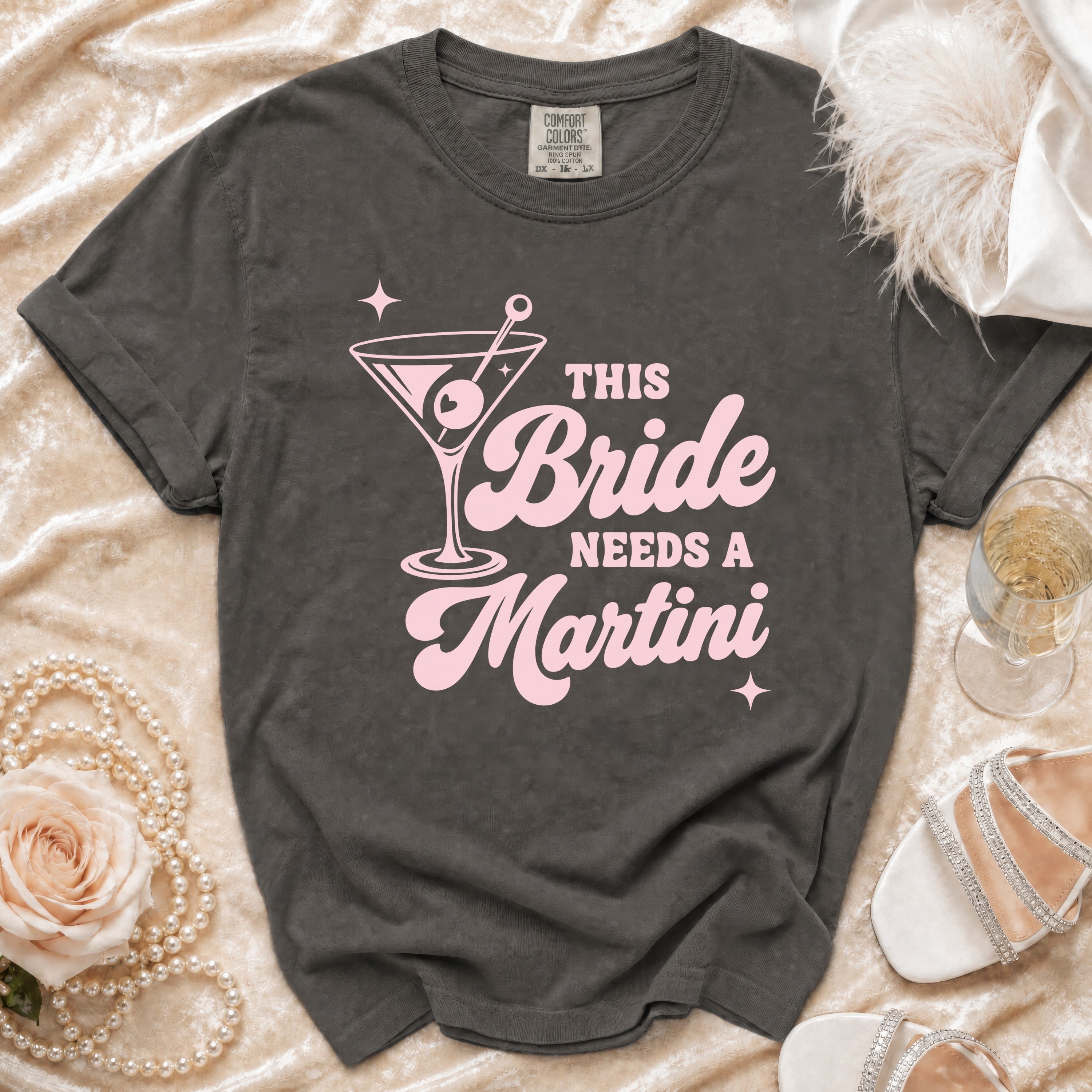 Dark gray t-shirt with pink text "This Bride Needs a Martini" and martini glass graphic.