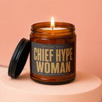 Amber candle with lit wick on pedestal, label reads "Official Title: Chief Hype Woman".