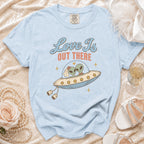 Light blue t-shirt with graphic of two aliens in a UFO, reading "Love Is Out There".